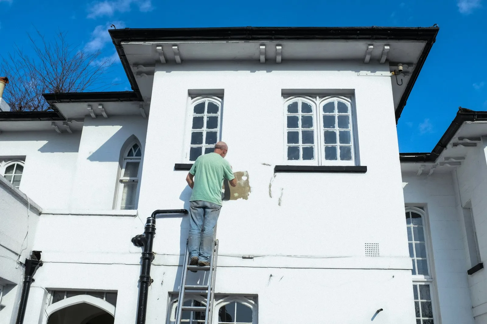 Maler streicht von der Leiter aus die Fassade eines weißen Hauses